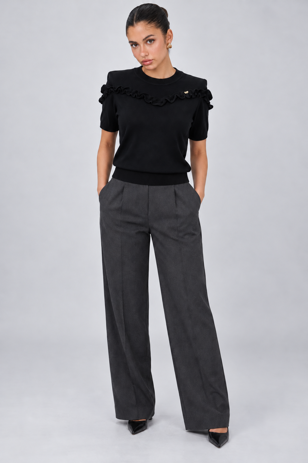 LIV0344AGI black ruffle top full front on model Maria, charcoal trousers