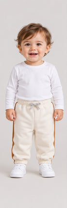Front view of boys' ivory baby sweatpants with caramel side stripes on an infant boy