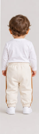 Back view of boys' ivory baby sweatpants with caramel side stripes on an infant boy